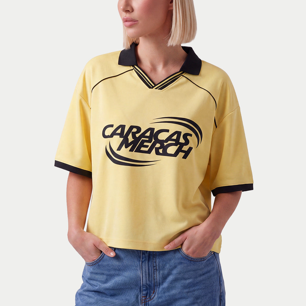 Mujer llevando la camiseta de fútbol boxy amarilla de Caracas Merch con vaqueros